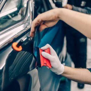 Car wrapping specialist putting vinyl foil or film on car. Selective focus.